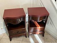 Two mahogany bedside tables side by side, showing fronts and tops with scalloped edges and carved legs.