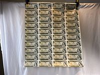 Full sheet of 40 uncut Canadian one dollar bills suspended by clips against white backdrop