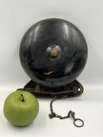 Front view of the antique black cast iron boxing bell with a green apple for size comparison.