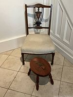 Full view of the antique wooden side chair with cushioned seat and the small wooden hand painted footstool in front.