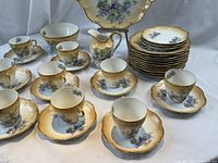 Full view of the china collection showing stacked plates, arranged teacups and saucers, serving plate in the background, and creamer.