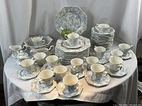Full set displayed on table: stacks of octagonal plates, piles of bowls, cups on small plates, sugar bowl with lid and gravy boat in front