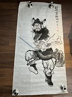 Full view of the scroll showing the warrior figure painted with brush and ink on light fabric or paper, secured at corners for photography.