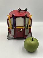 Front view of the ski gondola bird feeder with colorful ski poles and hanging loop, placed next to a green apple for size reference.