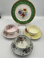 One photo showing four items: a porcelain plate with green border and floral center, and three tea cups with matching saucers in different floral patterns and colors.