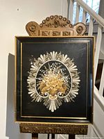 Full view of shadow box needlepoint showing floral beaded artwork in black and gold frame.