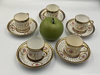 Overview of all five demi-tasse cups and saucers arranged around a green apple prop