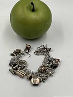 Charm bracelet with various detailed charms arranged on a table next to a green apple for size reference.