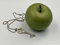 Sterling silver key pendant with quatrefoil cutout displayed with a green apple for size reference