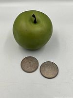 Two American silver dollar coins seen with a green apple for scale, showing front and back.