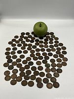 Green apple placed among approximately 120 coins for scale