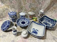 Overview of assorted oriental style ceramics on floral fabric background; includes jars, bowls, plates, small vases, and cups.