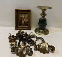 Overview of vintage brass drawer pulls, candle holder, and framed print of boy and dog on white surface