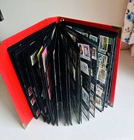 Red hard cover binder open, showing many pages of stamps mounted in plastic sleeves.