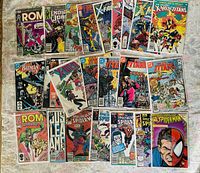 Set of 25 comic books laid out on a surface showing variety of superhero titles including ROM, Spectacular Spider-Man, New Teen Titans, X-Men, and Batman.