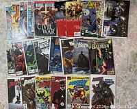 Photo showing 25 comic books including Daredevil, Civil War, Batman, Avengers, and Captain America titles laid out on a fabric surface.