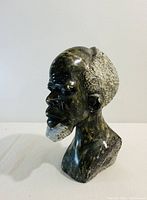 Front and side views of vintage African elder man bust carved from dark polished stone with rough textured hair and beard.