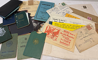 Wide view showing assorted vintage documents, certificates, envelopes, and small booklets with visible stamps and handwritten text.