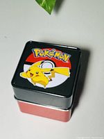 Closed square tin can showing Pokemon logo and Pikachu on lid.