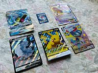 Photo showing five oversized Pokémon trading cards laid out together featuring Pikachu V, Dubwool V, Dragonite EX, Gyarados GX, Dragapult VMAX.