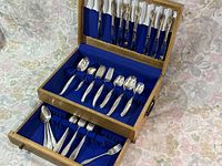 Wooden two-tier chest open showing 45 pieces of silverware including forks, spoons, and knives arranged neatly.
