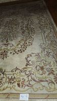 Close-up photo of a wool area rug showing detailed floral and scroll pattern with a traditional border. The rug appears worn and faded in areas.