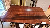Photo of solid wood dining table with two leaves, rectangular with visible wood grain finish and six chairs around it.
