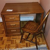 Photo of the wooden desk with three drawers and the Windsor style wooden chair placed next to it on a parquet floor.