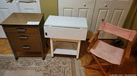 Wooden 3-drawer cabinet, white formica table on casters, and pink canvas director's chair shown together