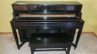 Front view of the vintage black Hardman upright piano with the bench positioned in front.