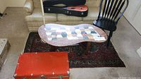 Overview of composite stone topped table, vintage red chest, guitar case, black wooden chair, and wool rug