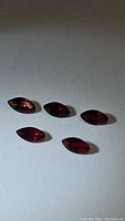 Five marquis cut rubies displayed on a flat surface, deep blood red color, clear clarity, shown from angled top view.