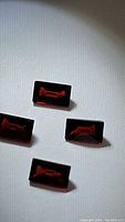 Four natural almandine garnet gemstones displayed on white surface showing their deep red color and baguette cut.