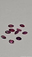 Photo showing ten marquise cut rubies arranged on a flat surface in close proximity, highlighting their rich pink to purple hues and facet reflections.