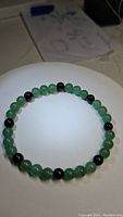 Full view of circular stretchy bracelet made of polished green aventurine and black onyx beads, displayed on white background.