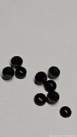 Photo of multiple small round cabochon jet black onyx stones laid out on a white background.