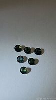 Seven round cut sapphires in various green and blue multicolored hues on plain background showing size and color variation.