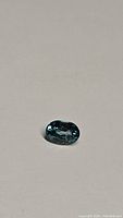 Photo shows an oval faceted natural Cambodian blue zircon gemstone on a neutral background, highlighting the lagoon blue color and clarity.