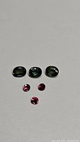 Photo of three oval green sapphires and three round rubies on white background