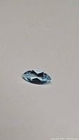 Close-up image of a natural marquis cut sky blue topaz gemstone placed on a plain surface, showing faceted surfaces and bright blue color.