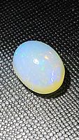 Close up photo of oval cabochon Ethiopian opal showing translucent body with color flashes of blue, aqua, green, and orange.