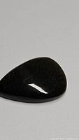 Front and top view of pear-shaped gold sheen obsidian cabochon gemstone showing smooth polished surface with golden flash sparkling within the dark black stone.