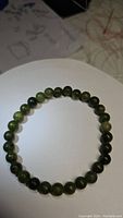 Photo showing the stretchy bracelet with round green jade beads laid flat in circular form on a white surface.