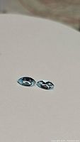 Pair of marquis-cut natural sky blue topaz gemstones placed side by side on a plain surface, showing their size and clarity.
