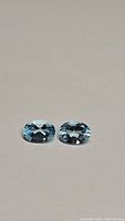 Pair of natural oval cut sky blue topaz gemstones shown on white background, highlighting their sky blue color and clarity.