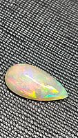 Close-up image of pear-shaped Ethiopian opal gemstone showing multicolored fire on textured black background