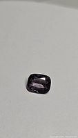 Close-up photo of a 1.47ct natural cushion cut purple spinel gemstone on a white background.