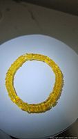Photo showing the circular stretchy bracelet made of small, polished golden yellow translucent Baltic amber beads placed on a white surface under direct light.