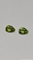 Two pear-shaped apple green peridot gemstones shown from front view against a plain light background.