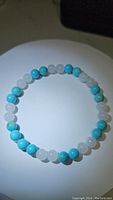 Top view of the turquoise and white jade bead bracelet on a white surface with shadow showing bead color and polish.